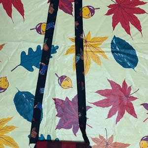 May include: A small crossbody bag featuring a red and black buffalo plaid pattern with a single button closure. The bag includes a long black strap decorated with a repeating pattern of small colourful boots and acorns.