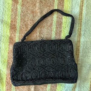 May include: A black beaded handbag with a handle. The bag features a geometric pattern and a clasp closure. The background is a striped fabric in shades of yellow, orange, and white.