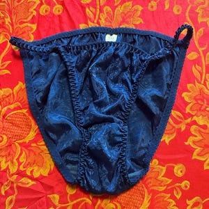Può includere: Mutandine blu navy con motivo floreale. La biancheria intima ha un bordo a balze e una lucentezza satinata. Lo sfondo è un tessuto rosso con un motivo floreale giallo.