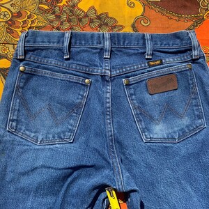 Puede incluir: Un par de pantalones vaqueros azules de mezclilla con un parche de cuero marr&oacute;n en el bolsillo trasero que dice "Wrangler".
