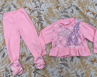 Puede incluir: Pijama rosa con una parte superior de manga larga y pantalones. La parte superior tiene un dobladillo con volantes y presenta un gráfico de zapatos de baile con el texto "Me encantan mis zapatos de baile".