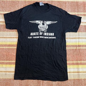 May include: Black t-shirt with a white graphic featuring a crest with wings and the text "ABATE OF INDIANA (LET THOSE WHO RIDE DECIDE)". The shirt is made of a soft material and has a crew neck.