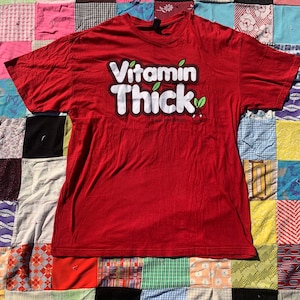 May include: Red t-shirt with a white graphic that says "Vitamin Thick" with a green leaf and a red cherry. The text below the graphic says "It was all a dream."
