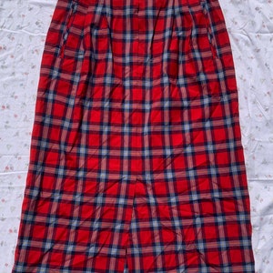 May include: A red, blue, and yellow plaid skirt with a front slit. The skirt has a high waist and is pleated.