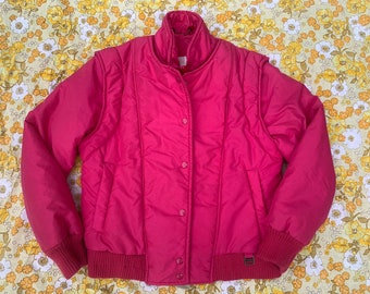 May include: A pink quilted jacket with a zipper closure and button accents. The jacket has a ribbed collar, cuffs, and hem.