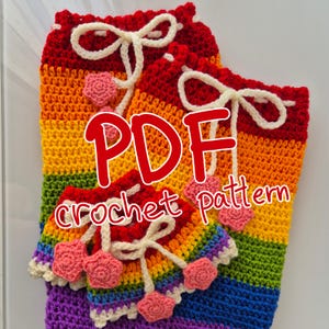 Puede incluir: Un conjunto de bolsas de ganchillo a rayas arcoíris con cordones blancos y adornos rosas en forma de corazón. Las bolsas muestran el texto "PDF crochet pattern" en rojo.