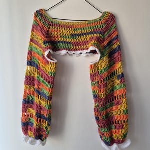 May include: A colorful crochet top with long sleeves. The top features a rainbow of colors including orange, yellow, green, and purple. The sleeves and the bottom of the top are trimmed with white crochet.