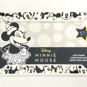 May include: White plastic license plate frame with a black and white image of Minnie Mouse. The frame is decorated with a polka dot pattern and multiple images of Minnie Mouse's face. The text "Disney Minnie Mouse" is printed on the frame. The text "Auto Frame Cadre Pour Auto Marco Para Coche" is printed on the frame.
