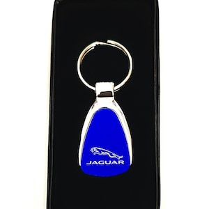 May include: A silver key chain with a blue, teardrop-shaped charm featuring a white Jaguar logo and the word "JAGUAR" in white lettering.