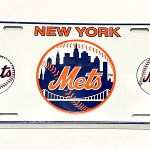 May include: White metal New York Mets license plate featuring the team logo with a baseball, a skyline, and a bridge. The logo is in orange, blue, and white. The words "New York Mets" are printed in blue.