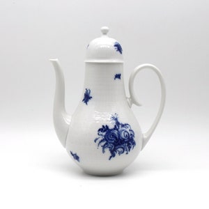 Puede incluir: Cafetera de porcelana blanca con cuerpo alto y cilíndrico, boquilla curva y asa de bucle. La cafetera está decorada con patrones y detalles florales azules. La tapa tiene un pequeño pomo. Una pieza clásica para servir café.
