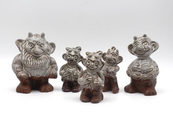 May include: A collection of ceramic troll figurines. The trolls have gray bodies and brown bases. The trolls have various facial expressions and poses. The figurines are displayed on a white background.