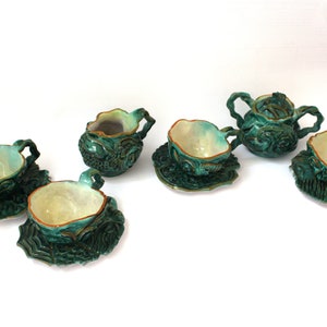 Può includere: Un set da tè in ceramica verde acqua con intricati disegni floreali. Il set comprende una teiera, un creamer e quattro tazze da tè e piattini.