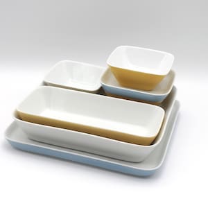 May include: A stack of rectangular and square ceramic serving dishes in various sizes. The dishes have white interiors and are accented with yellow and light blue rims. The set includes a large tray, a long rectangular dish, and several smaller bowls.