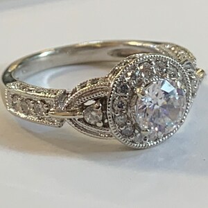 Puede incluir: Un anillo de plata con una gran piedra redonda central rodeada de piedras m&aacute;s peque&ntilde;as. La banda est&aacute; decorada con detalles intrincados.