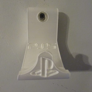 May include: White plastic wall mount for a Playstation 5 console. The mount has a screw hole at the top and the Playstation logo embossed on the front.