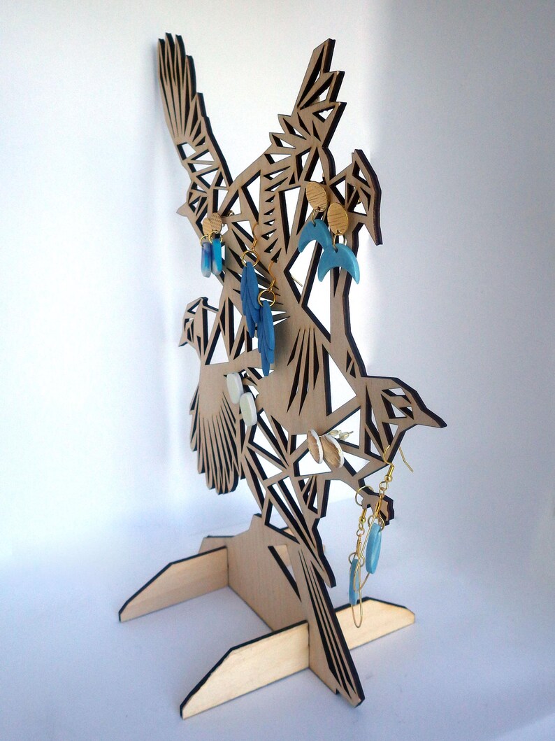 Puede incluir: Soporte para pendientes de madera con forma de p&aacute;jaro con patrones geom&eacute;tricos. El soporte tiene una base y est&aacute; decorado con pendientes azules y dorados.