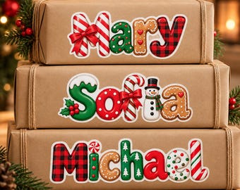 May include: Three stacked brown paper gift boxes featuring festive holiday-themed name stickers. The top box reads Mary, the middle box reads Sofia, and the bottom box reads Michael, all decorated with candy cane, gingerbread, and plaid patterns.