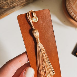 May include: A brown leather bookmark with a gold tassel and a gold ring. The bookmark has the text "Moments Together" printed on it.