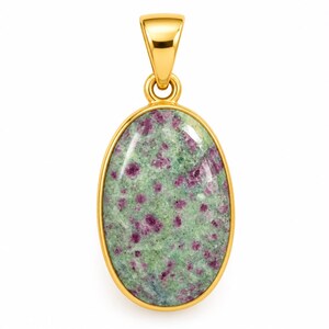 Puede incluir: Un colgante ovalado que presenta una piedra de zoisita verde pulida con inclusiones de rubí magenta incrustadas, engastado en un marco de oro amarillo liso con una anilla de oro a juego en la parte superior para una cadena.