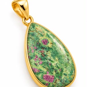 Pode incluir: Um pingente em forma de gota com uma pedra de zoisite verde polida e inclusões de rubi magenta. A gema está engastada numa estrutura de metal dourado liso e brilhante, com uma argola a condizer no topo para a sua suspensão.