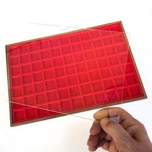 Può includere: Una teca in legno con interno in velluto rosso e coperchio in acrilico trasparente. La teca ha 100 scomparti individuali per riporre piccoli oggetti.