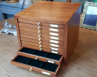 Op de afbeelding: Een houten doos met 10 laden, elk met een klein label. De laden zijn open, waardoor een groene fluwelen voering zichtbaar is. De doos is gemaakt van donker hout met een natuurlijke afwerking.