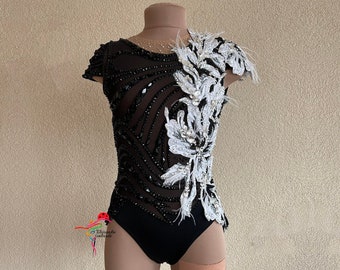May include: Black leotard with a white feathered design on the right side. The leotard is embellished with rhinestones and sequins.