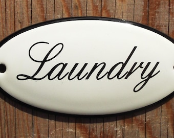 May include: White oval sign with a black border and the word "Laundry" written in a black cursive font.
