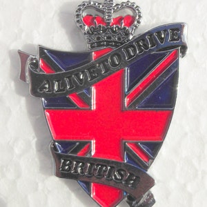 Op de afbeelding: Een zilveren metalen pin met een rood, wit en blauw Union Jack-ontwerp. De pin heeft een banner met de tekst "Alive to Drive" en een andere banner met de tekst "British". De pin heeft ook een zilveren kroon bovenop.