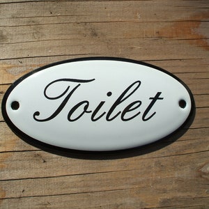 Letrero clásico de baño esmaltado. Texto negro sobre fondo blanco, forma ovalada. 10 x 5 cm.