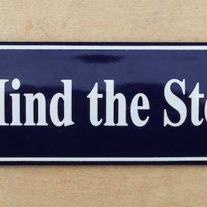 May include: A blue enamel sign with white lettering that reads "Mind the Step".