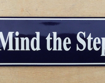 Classic Enamel 'Mind the Step' sign. White text on a blue background. 19x6cm.