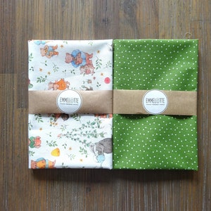 May include: Four fabric squares, two with whimsical animal and floral patterns, and one with white polka dots on a green background. Each set is wrapped with a brown paper band featuring the "EMMELOTTE" logo.