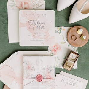 May include: A wedding invitation suite with a watercolor floral design. The invitation card features a pink and white watercolor background with the text "Save Our New Date" and the couple's names, "Stephanie and Keith". The date, "06.27.20", and location, "Atlanta, Georgia", are also included. The RSVP card features the text "Kindly respond on or before May tenth" and options to indicate whether the guest will attend or not.
