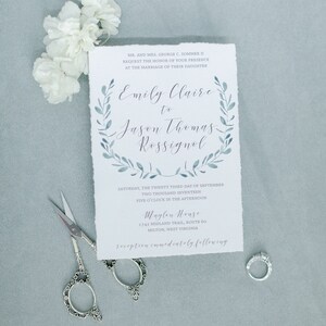 May include: A wedding invitation with a watercolor wreath design in shades of blue. The invitation announces the marriage of Emily Claire to Jason Thomas Rossignol on September 23, 2017, at 5:00 PM at Maglen House, 1742 Midland Trail, Route 60, Milton, West Virginia. The reception will immediately follow.