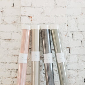 May include: Four rolls of fabric in clear plastic tubes. The fabric colors are pink, beige, gray, and green. Each tube has a white label with the text "Olive & Oak" printed on it.