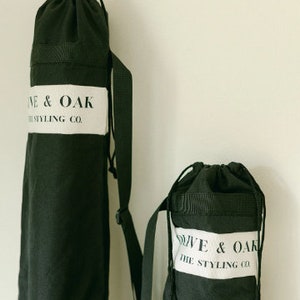 May include: Two black canvas bags with adjustable straps. The larger bag has the text "Olive & Oak The Styling Co." printed on a white label. The smaller bag has the same text printed on a white label.