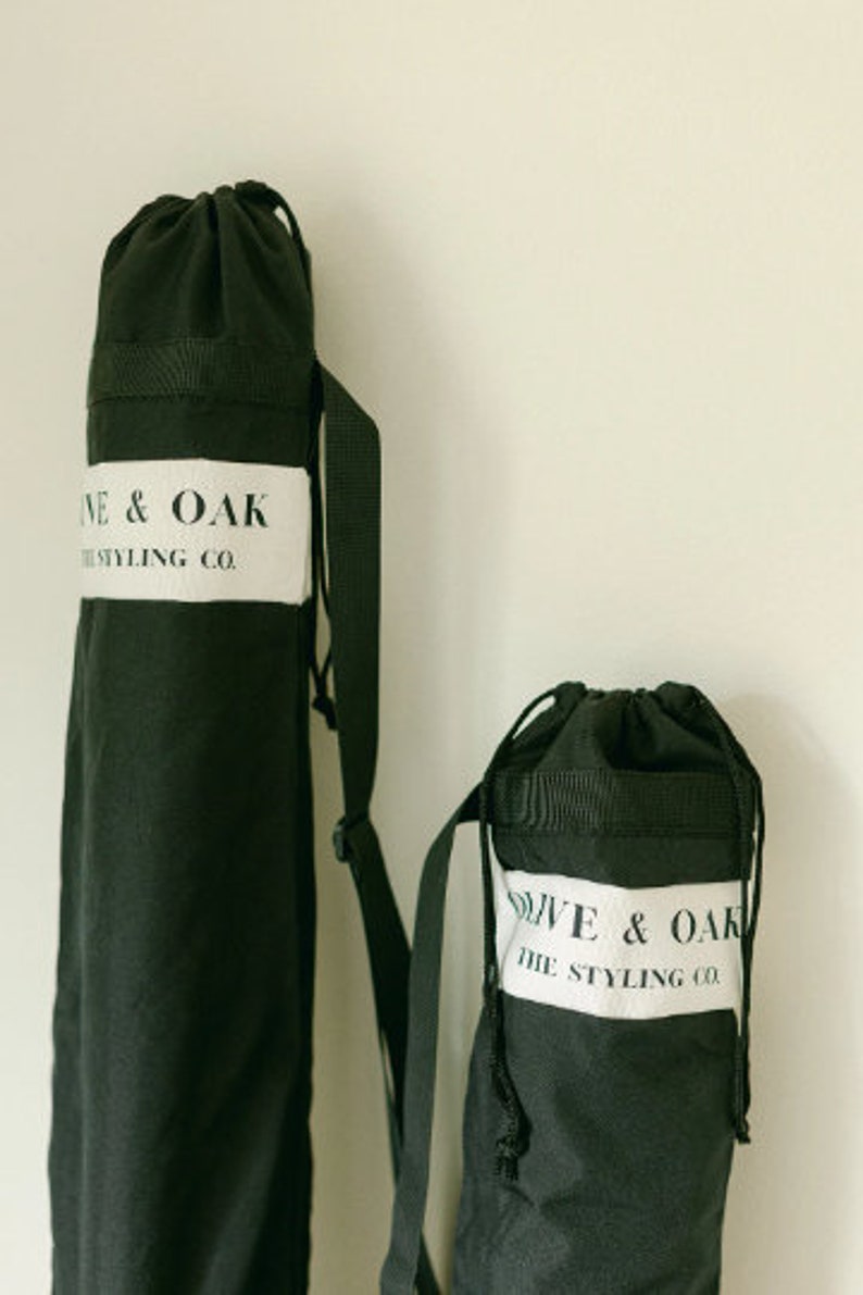 May include: Two black canvas bags with adjustable straps. The larger bag has the text "Olive & Oak The Styling Co." printed on a white label. The smaller bag has the same text printed on a white label.