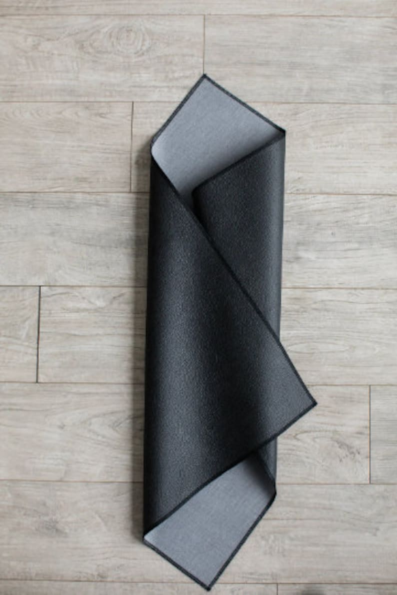 May include: A black and gray yoga mat is folded in half and laid flat on a light wood floor.