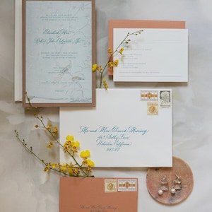 May include: A wedding invitation suite with a blue and white floral design. The invitation is on a brown paper background. The RSVP card is on a peach background. The envelope is white with blue calligraphy. The return address is on a peach envelope. The text on the invitation reads "Elizabeth Ann and Robert John Calcagno, Jr."