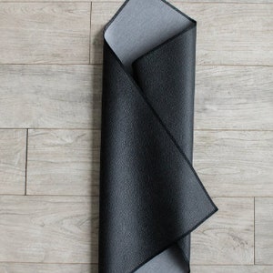 May include: A black and gray yoga mat is folded in half and laid flat on a light wood floor.