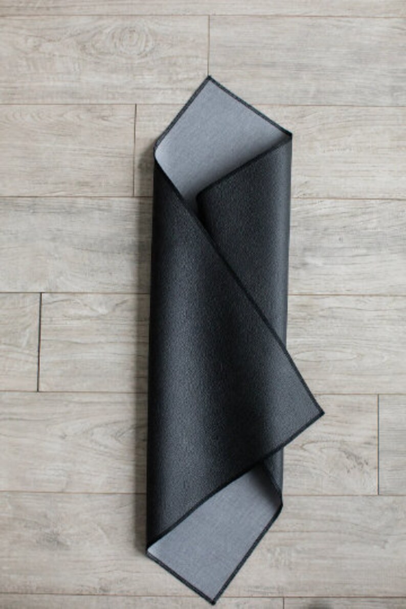 May include: A black and gray yoga mat is folded in half and laid flat on a light wood floor.