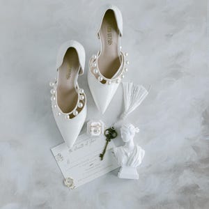 May include: A pair of white bridal shoes with pearl embellishments, a small box with rings, a key, and a white statue of a woman's bust. The invitation reads "The eleventh of June".