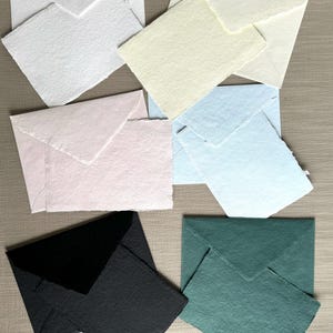 May include: Six different colored envelopes with a textured paper finish. The envelopes are in shades of white, cream, pink, blue, black, and green.