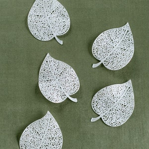 May include: Five white, delicate, paper leaves with intricate patterns are arranged on a green background.