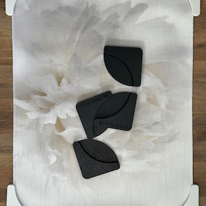 May include: Three black corner protectors with the text "OLIVE & OAK" and "MATTRESSES" on them. The protectors are on a white tablecloth with a floral pattern.