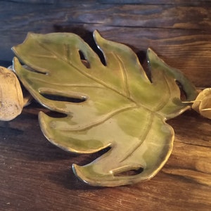 May include: A ceramic leaf-shaped dish with a green glaze. The dish has a detailed design of a monstera leaf.
