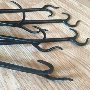 Peut inclure: Quatre outils de cheminée en métal noir avec des poignées courbes et des crochets. Les outils sont disposés en rangée sur une surface en bois.