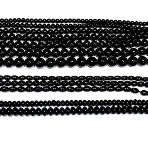 Könnte beinhalten: Reihenweise schwarze Edelsteinperlen in verschiedenen Größen. Die Perlen sind rund und oval, mit glänzender Oberfläche. Die Perlen sind aufgefädelt und eignen sich für die Schmuckherstellung oder andere Bastelprojekte.